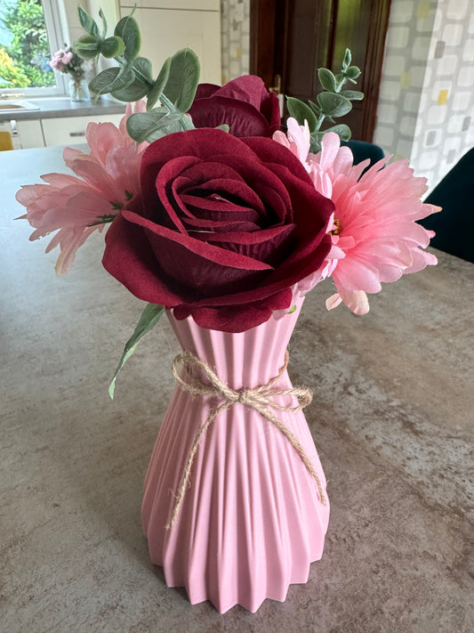 Two deep red roses with baby pink daisies in a beautiful ripples pink vase